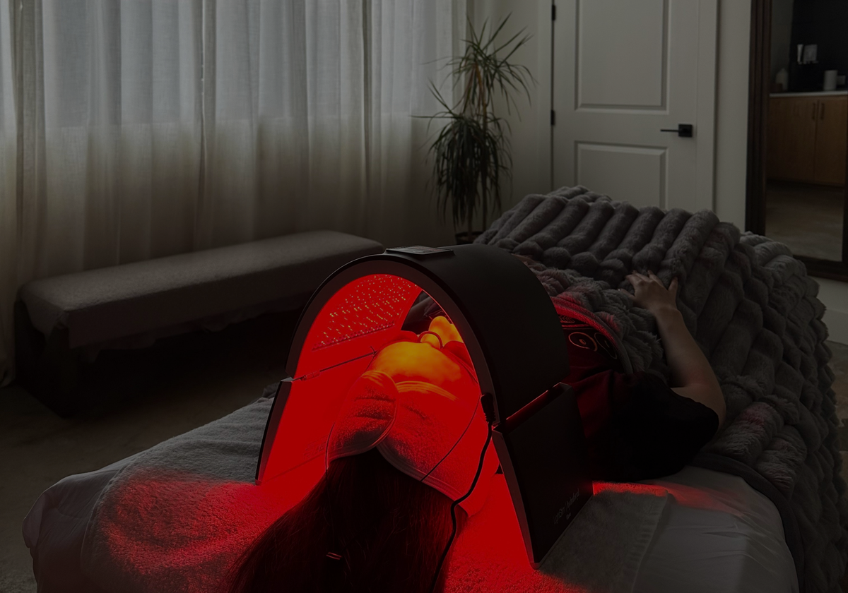 A person receiving a facial, using a red light therapy mask to stimulate collagen and reduce inflammation.