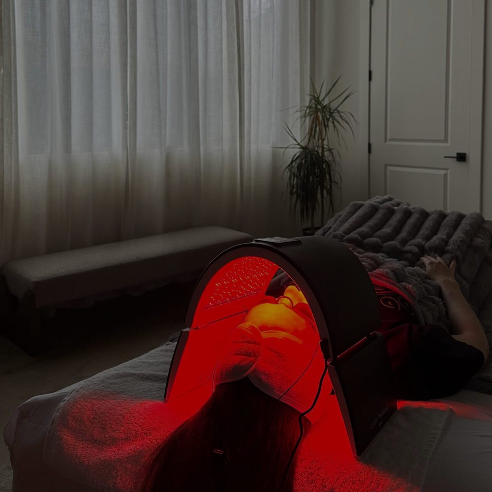 A person receiving a facial, using a red light therapy mask to stimulate collagen and reduce inflammation.